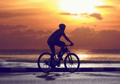 Silhouette man riding bicycle by sea against sky during sunset