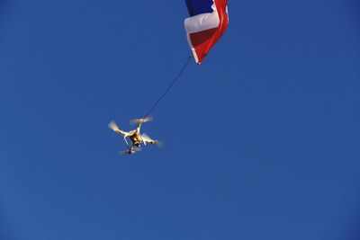 Low angle view of drone flying with flag against clear blue sky