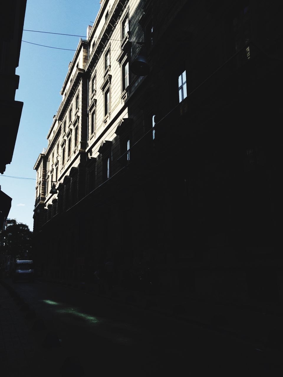 building exterior, architecture, built structure, clear sky, low angle view, street, building, city, street light, road, residential building, sky, residential structure, transportation, outdoors, shadow, the way forward, no people, car, city street