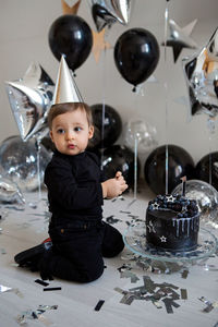 Boy stands next to a festive black cake and balloons