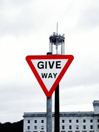 Give way sign with street light against cloudy sky