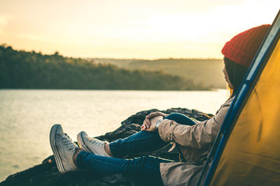 Low section of man relaxing on lake at sunset