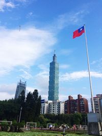 Low angle view of flag by skyscrapers in city against sky