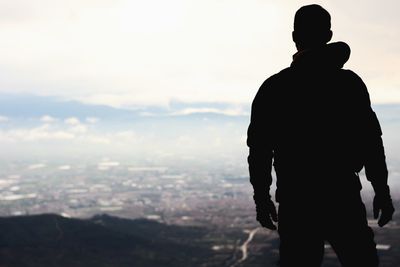 Rear view of silhouette man looking at cityscape against sky
