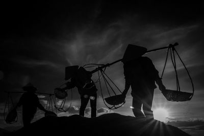 Silhouette people working against sky during sunny day