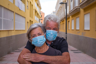 Portrait of couple wearing mask in alley amidst buildings