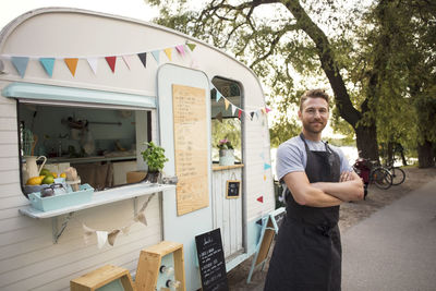 Portrait of confident owner standing arms crossed outside food truck on street