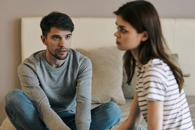 Young man looking at girlfriend while sitting pn bed at home