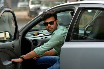 Young man getting out from car at street in city