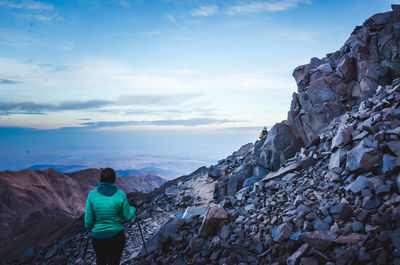 Rear view of man standing on rock against sky