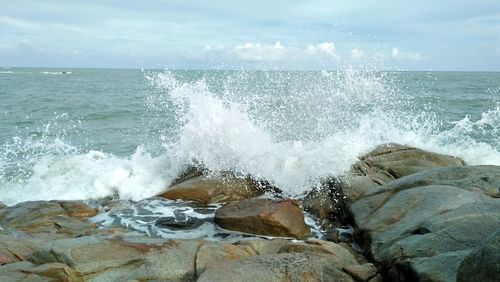 Waves splashing on rocks at shore against sky