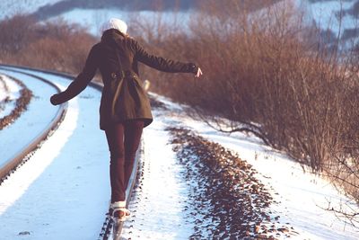 Rear view of woman walking on snow covered railroad tracks