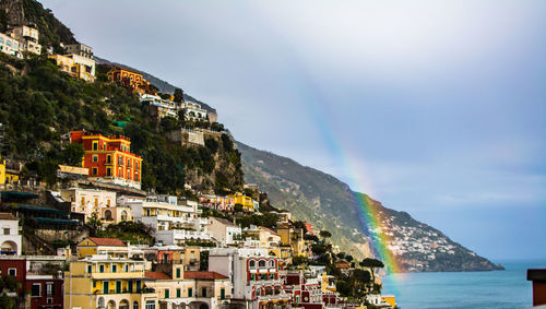 Scenic view of rainbow over town by sea against sky