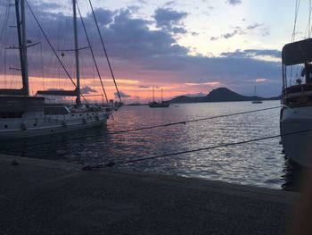 Sailboats moored on sea against sky during sunset