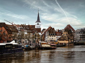 Buildings by river against sky in city