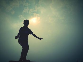 Silhouette boy dancing against sky during sunset
