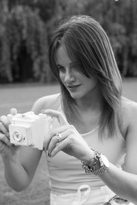 Smiling young woman holding toy camera on land