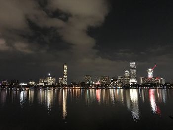 Illuminated buildings by river against sky at night