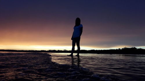 Silhouette woman standing in lake against sky during sunset