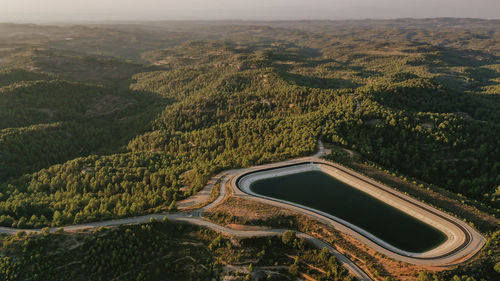 Aerial view of mountaintop reservoir at dusk with forested hills in background