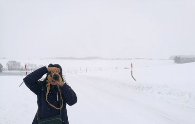 Woman photographing on snow covered field against sky