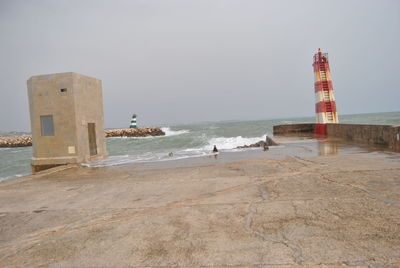 Lighthouse on beach by sea against sky