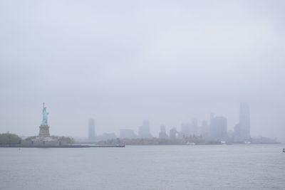 Statue of liberty by sea against sky in foggy weather