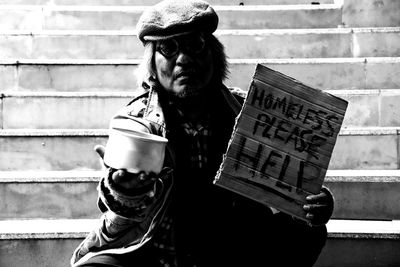 Portrait of mature man with placard begging on steps