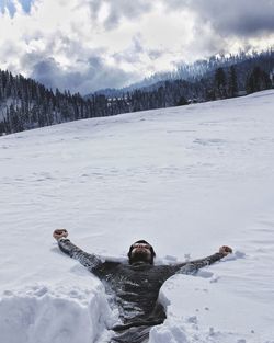 Man with arms outstretched lying on snow covered land
