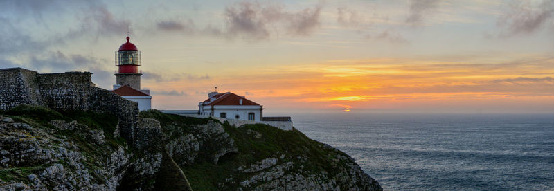 Lighthouse by sea against sky during sunset