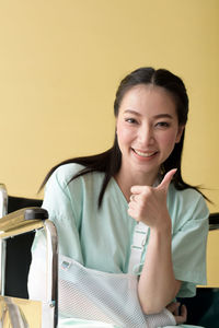 Portrait of smiling disabled woman sitting on wheelchair against wall