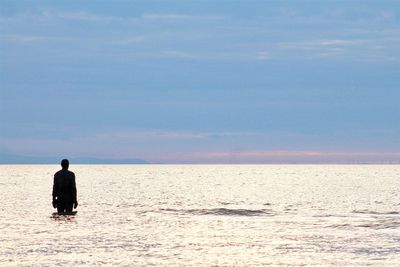 Silhouette man standing in sea against sky during sunset