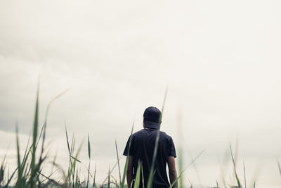 Rear view of man walking amidst grass against cloudy sky