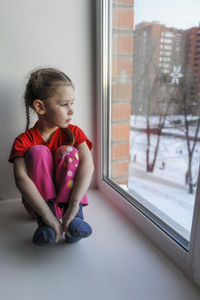 Girl looking away while sitting on window