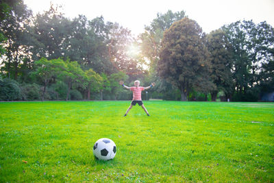 Woman playing soccer ball on grass against trees