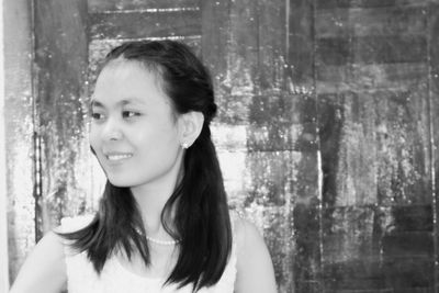 Close-up of smiling young woman looking away while standing against door