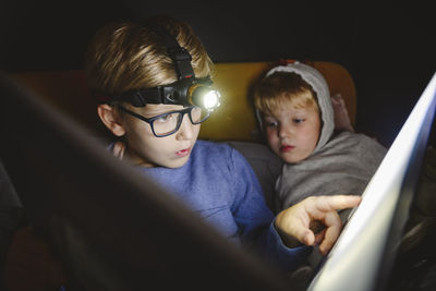 Boy wearing headlight reading book with brother at home