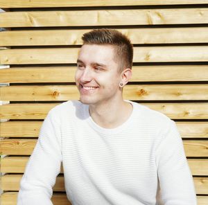 Smiling young man against wooden wall