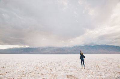 Rear view of woman with hand raised standing on sand at desert