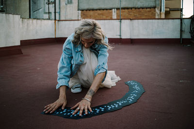 Serious female fortune teller reading tarot cards while sitting on roof of old building