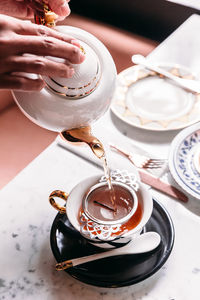 High angle view of cropped hand pouring tea from kettle in cup on table