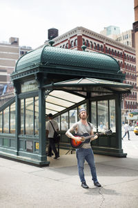 Man playing guitar while standing on street in city