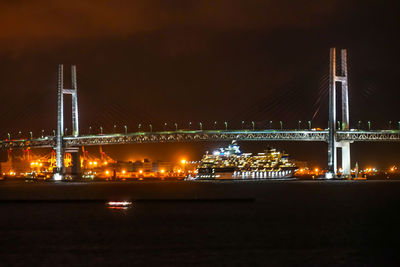 Illuminated bridge over river against sky at night