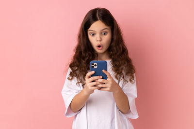 Young woman using mobile phone while standing against pink background