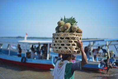 Man carrying pineapples in wicker basket at beach