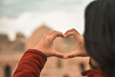 Woman making heart shape against sky