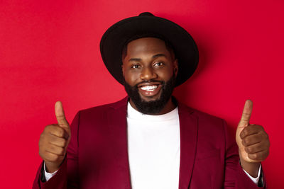 Portrait of young man wearing hat standing against red background