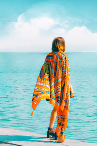 Woman with scarf standing at beach against sky