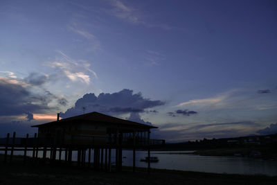 Silhouette house by sea against sky during sunset