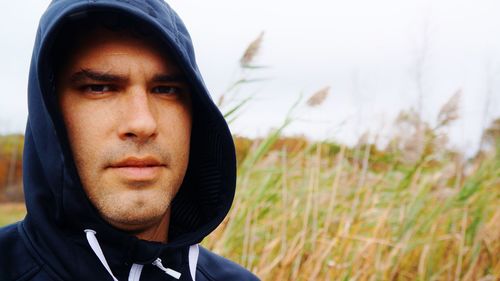 Close-up portrait of man wearing hooded shirt on field against sky